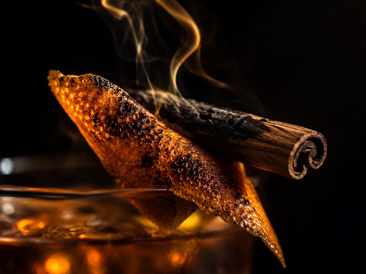 Close up of the charred orange twist and smoking cinnamon stick garnish on the Outlaw King whiskey sour