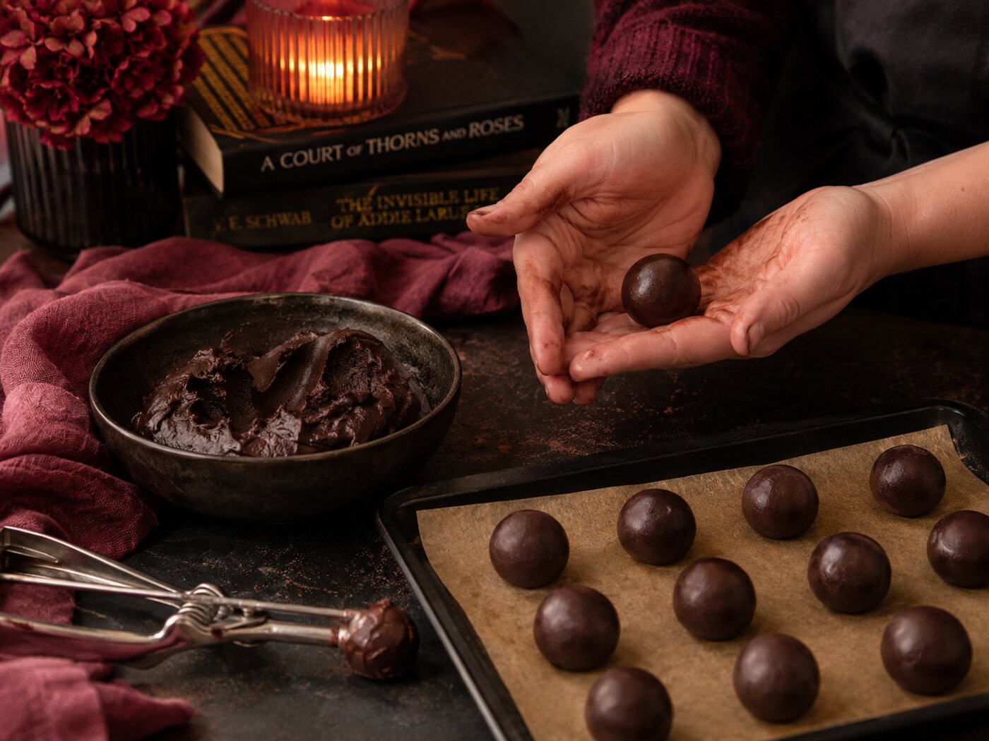 Rolling a chilled ganache ball between cupped palms, with a tray of finished balls alongside.