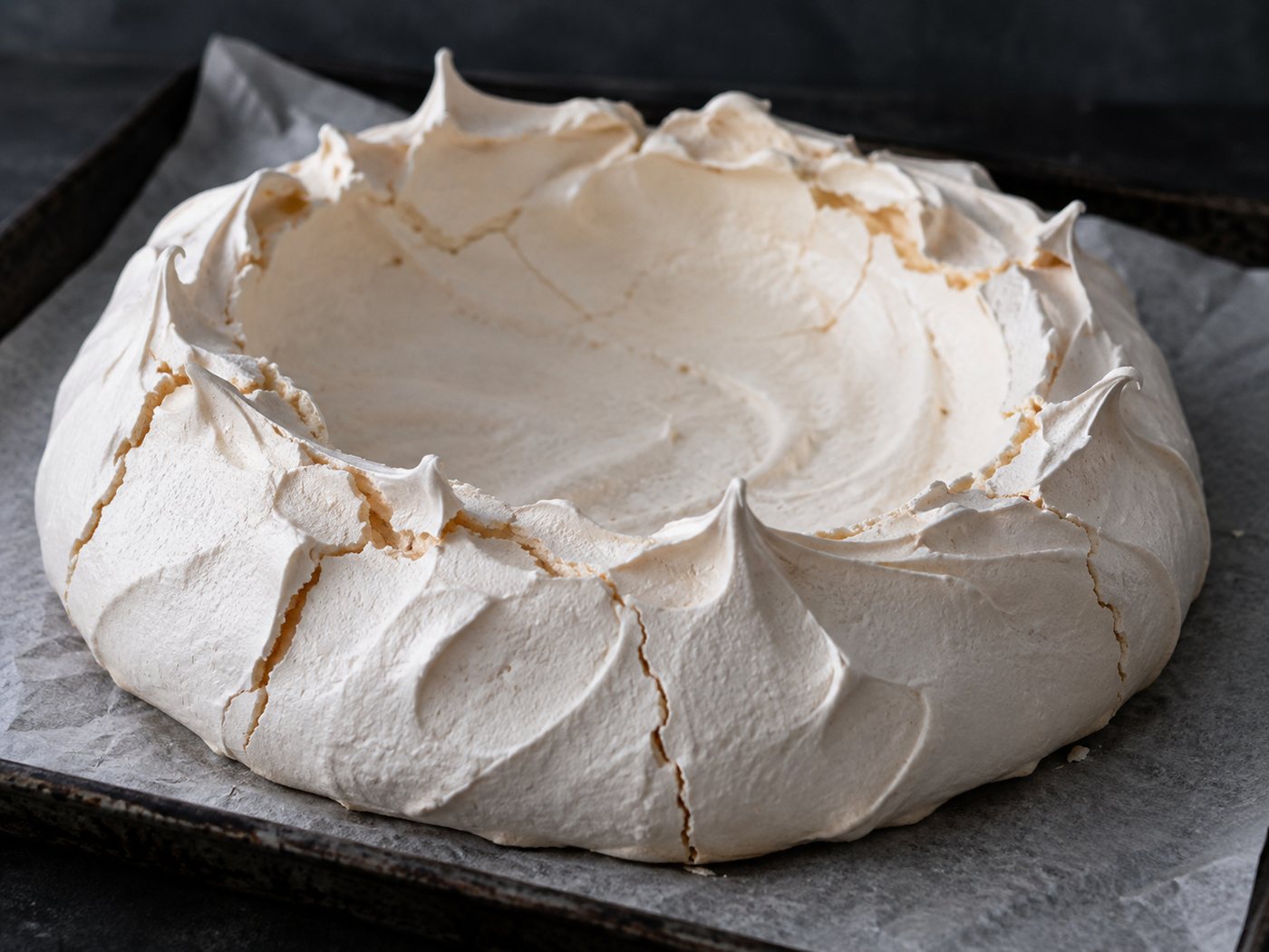 A baked and cooled pavlova shell, pale and lightly cracked, with a sunken crater in the centre