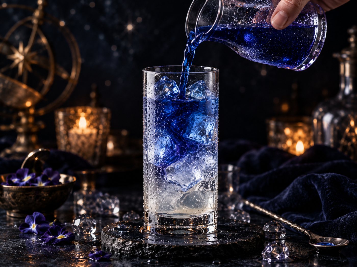 Deep blue butterfly pea tea being poured from a jug into a tall glass packed with ice