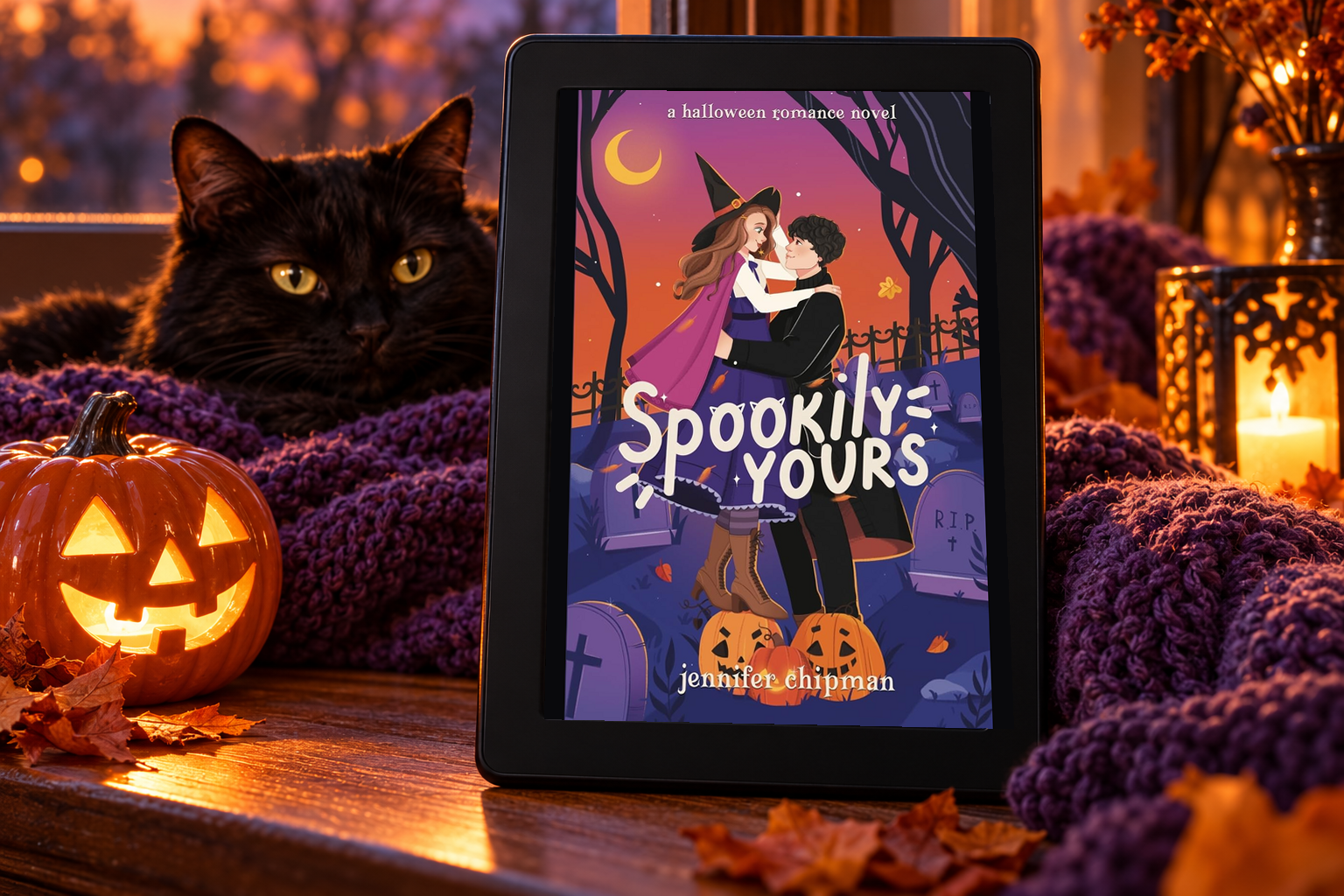 Spookily Yours on a Kindle beside a black cat, pumpkin and purple blanket.