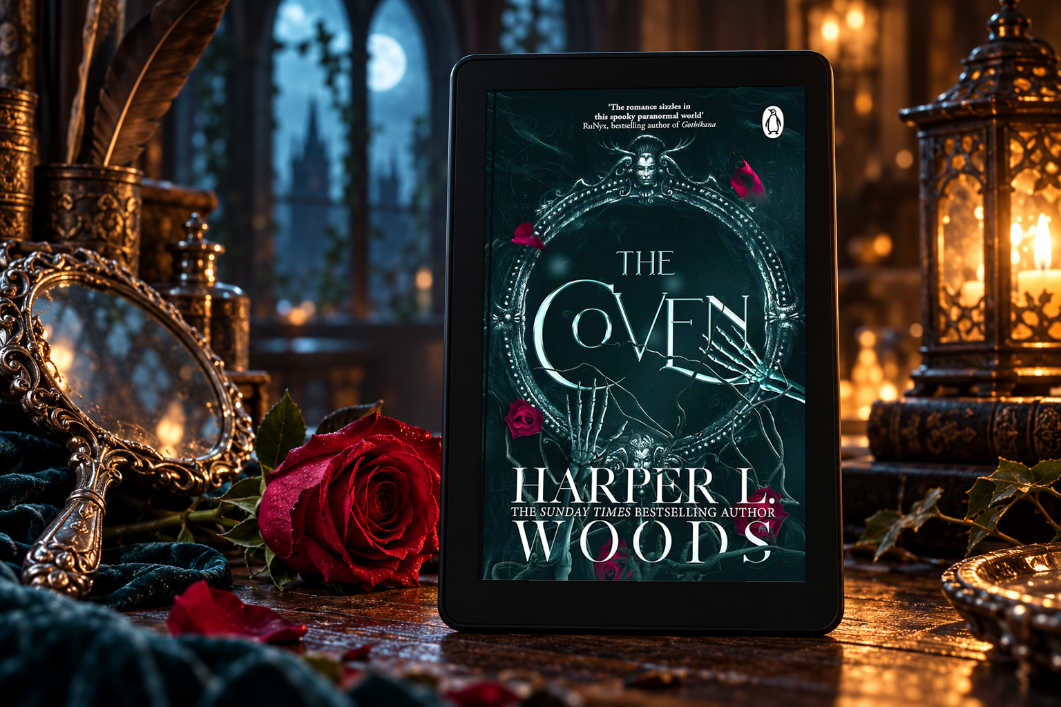The Coven on a Kindle beside an ornate mirror and red rose in a gothic study.