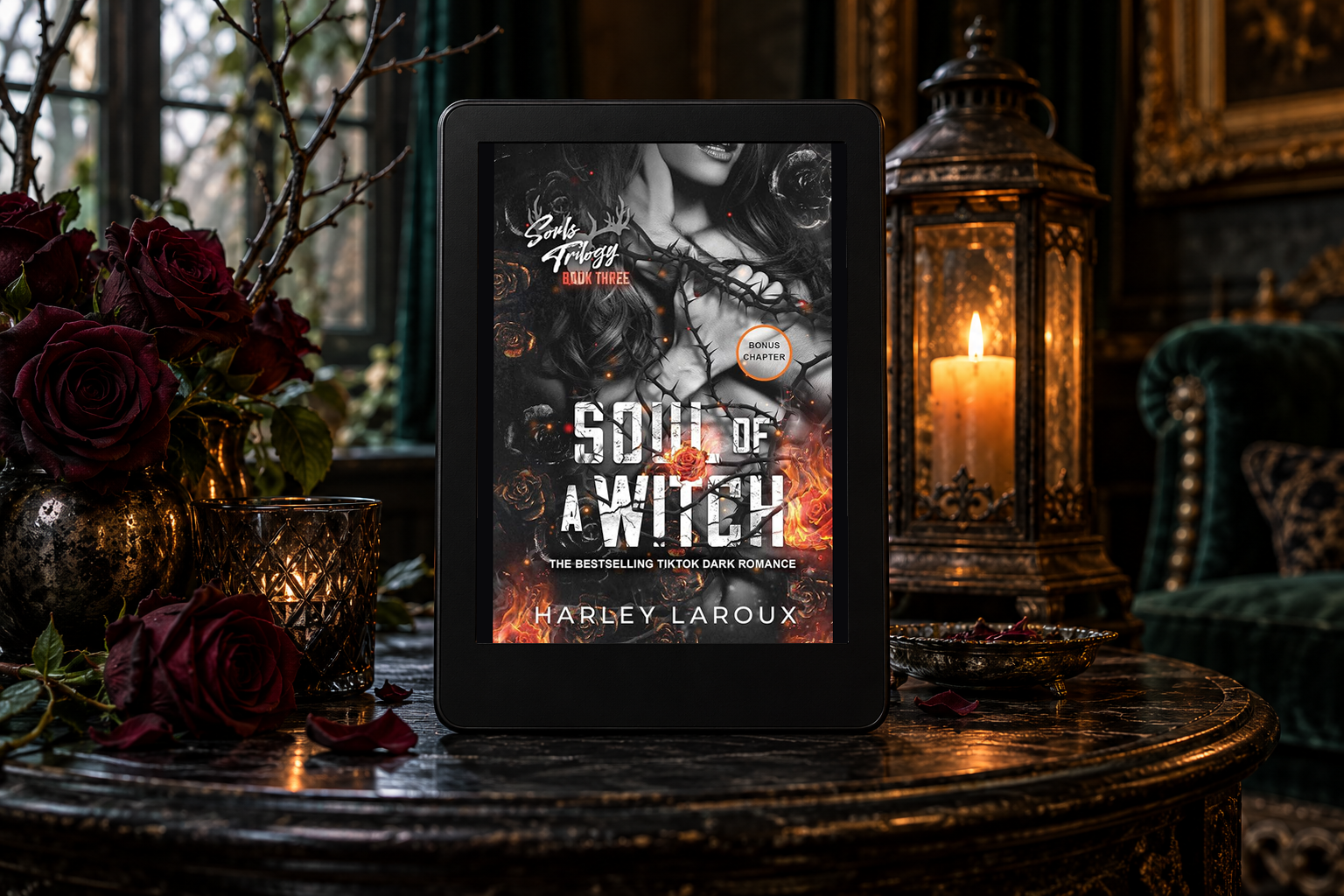 Soul of a Witch on a Kindle beside dark roses and a lantern in a shadowy room.